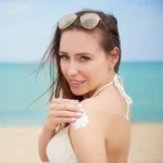 Woman applying sunscreen on beach in UAE for skin protection